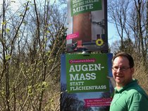 Wahlkreiskandidat Jan Karthäuser hängt ein Plakat auf. Text: Augenmaß statt Flächenfraß, 6. Mai, Wählen! Mit beiden Stimmen Grün den Mückenwald erhalten.